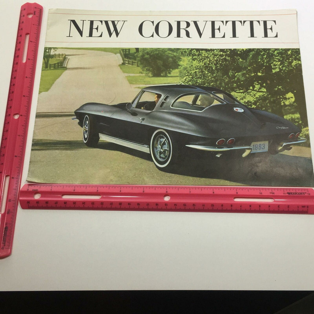 Cover page of the 1963 New Corvette Sting Ray Sport Coupe Sale Brochure, depicting a black Corvette parked on a road with a lush landscape in the background.