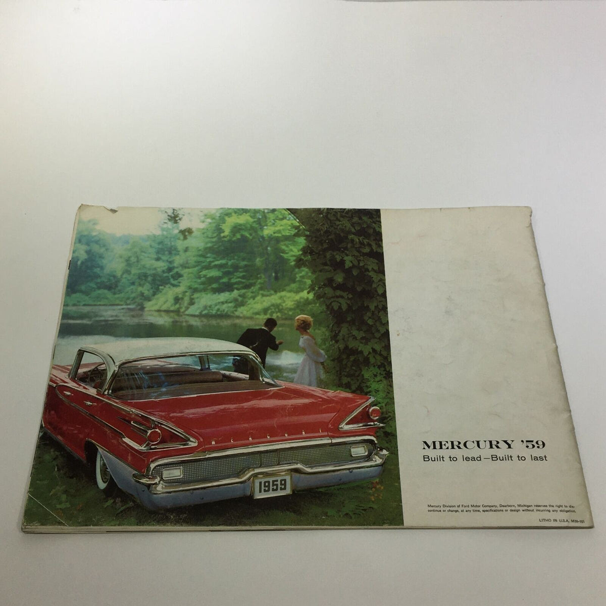 The back cover of the 1959 Mercury America's Liveliest Luxury Car Monterey 2-Door Sedan Car Brochure, depicting a red Mercury car by a scenic river with a couple, emphasizing the elegance of the vehicle.