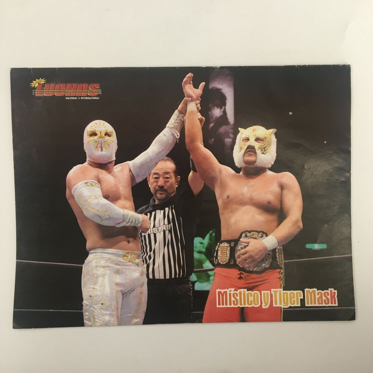 Image from Super Luchas Magazine November 2009 showcasing Místico and Tiger Mask, celebrating a victory with a referee in the ring.