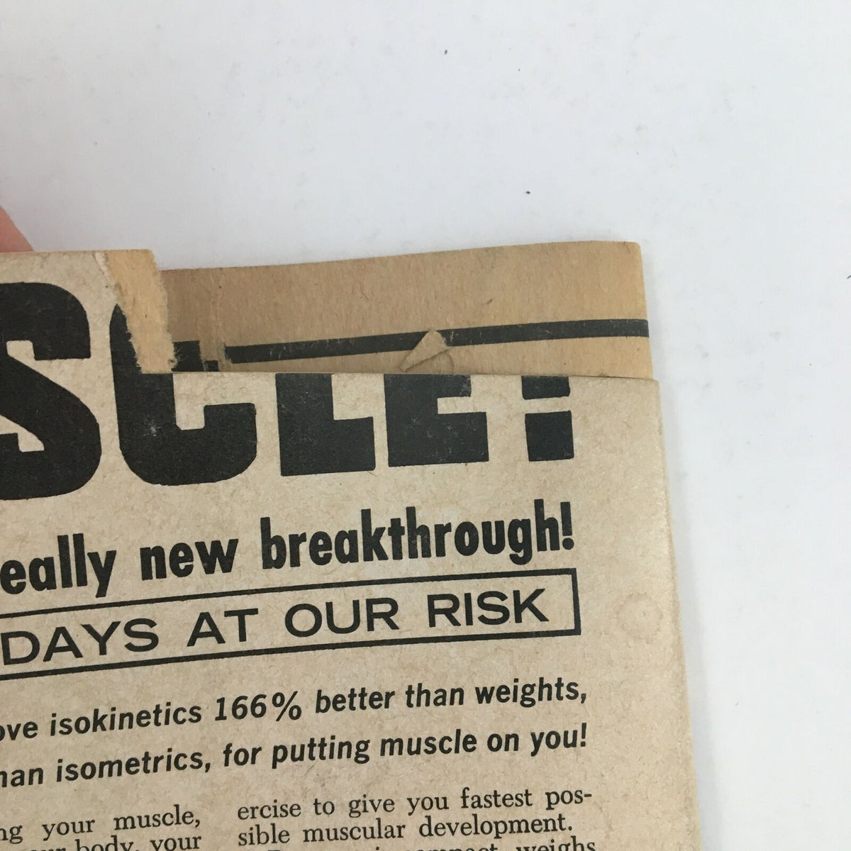 Close-up view of a damaged corner of the Wrestling Revue Magazine from October 1974, featuring the title and advertisement for muscle-building techniques. This issue highlights the match between Bruno Sammartino and Jonathan, showcasing its vintage appeal.