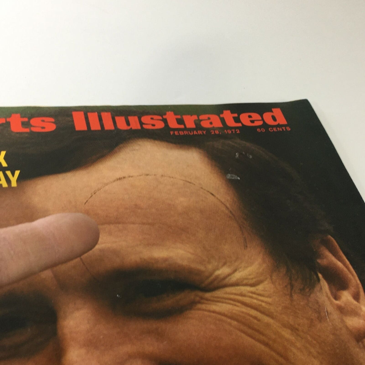 Close-up of the Sports Illustrated magazine cover from February 28, 1972 showing Super Tex Runs Away with Daytona, highlighting a mark and showing a finger pointing at the cover.
