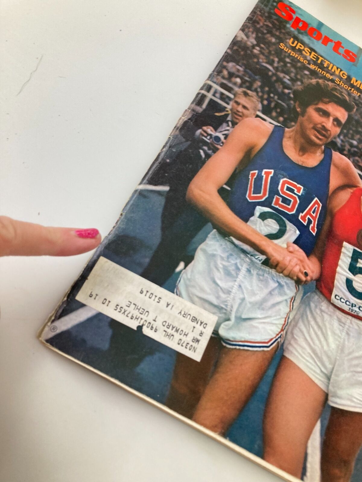 Detailed view of the August 3, 1970, Sports Illustrated magazine cover showing Frank Shorter consoling Leonid Mikitenko after a meet in Leningrad, with a price label visible on the bottom.