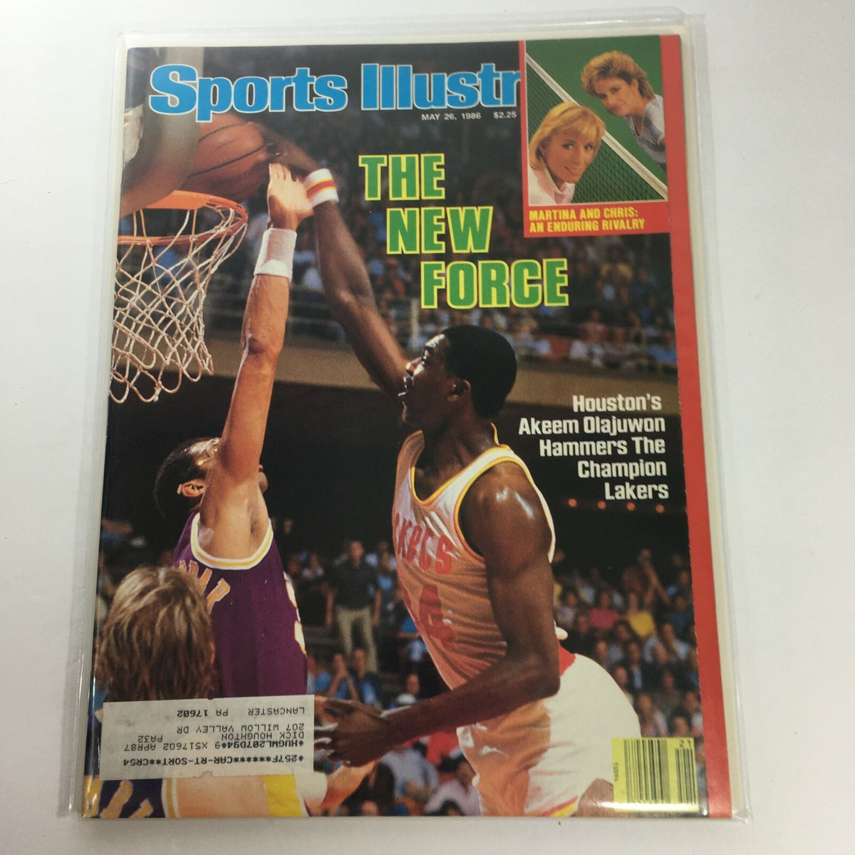 Sports Illustrated magazine cover from May 26, 1986, featuring Houston's Akeem Olajuwon as he makes a powerful play against the Lakers. The headline reads 'The New Force' highlighting Olajuwon's impact in basketball. The magazine is in excellent condition, bagged and boarded for protection.