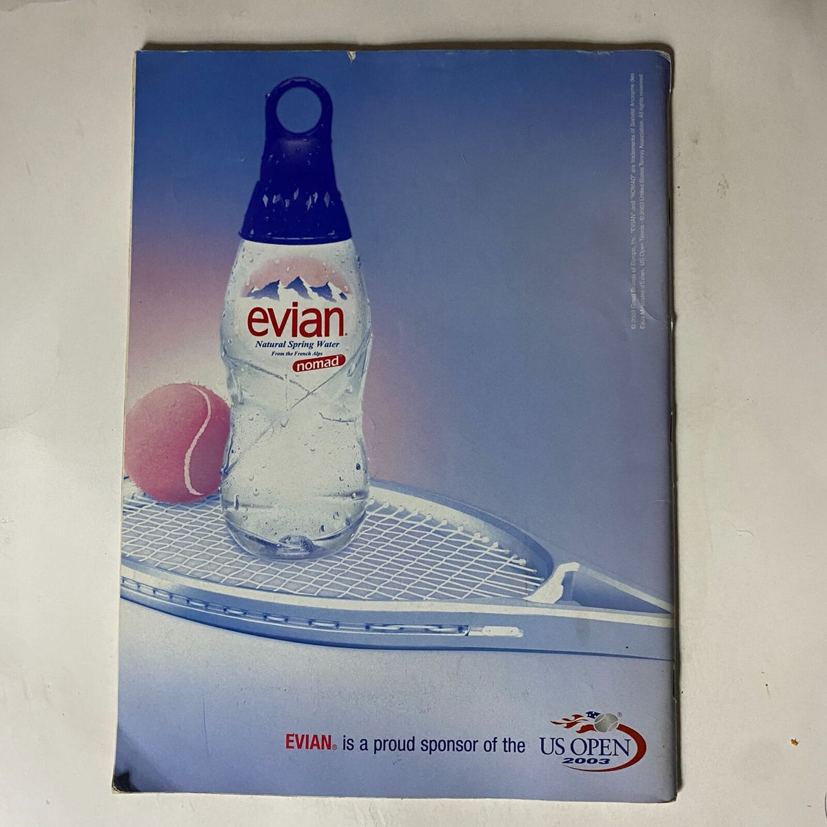 Evian water bottle featured in Tennis Magazine August 2003 issue with Pete Sampras and Andre Agassi on the cover. Promoting hydration, this image showcases Evian as a proud sponsor of the US Open 2002, complementing the focus on tennis culture.
