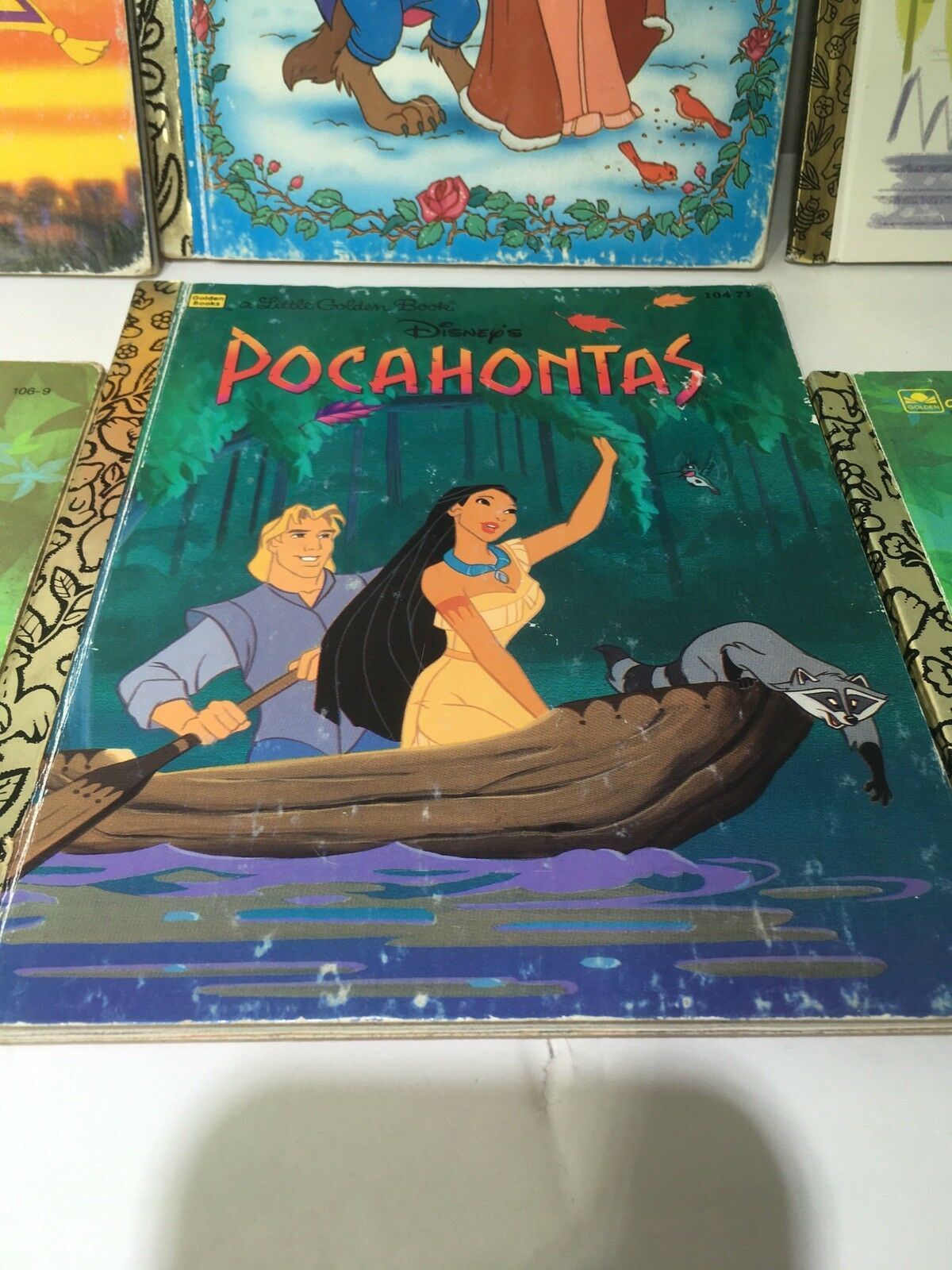 Little Golden Book Disney Pocahontas depicting Pocahontas and John Smith in a canoe, with a raccoon in the foreground, showcasing a beloved Disney story.