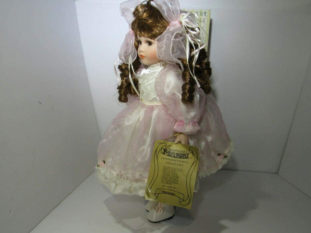 SEYMOUR MANN 'SALLY' Connoisseur Collection doll displayed in a pink dress, showcasing the doll's intricate details and curly hair.