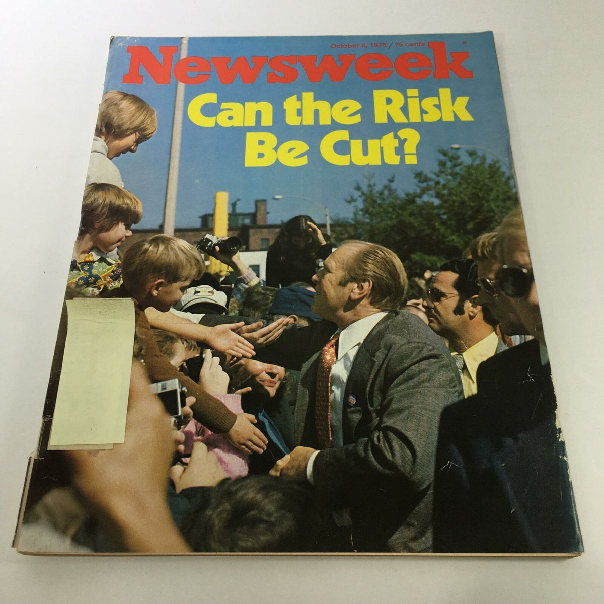 Cover of Newsweek Magazine: October 6, 1975 featuring the title 'Can The Risk Be Cut?' with a scene of a politician shaking hands with children and a crowd in the background, showcasing elements of historical journalism and vintage magazine appeal.