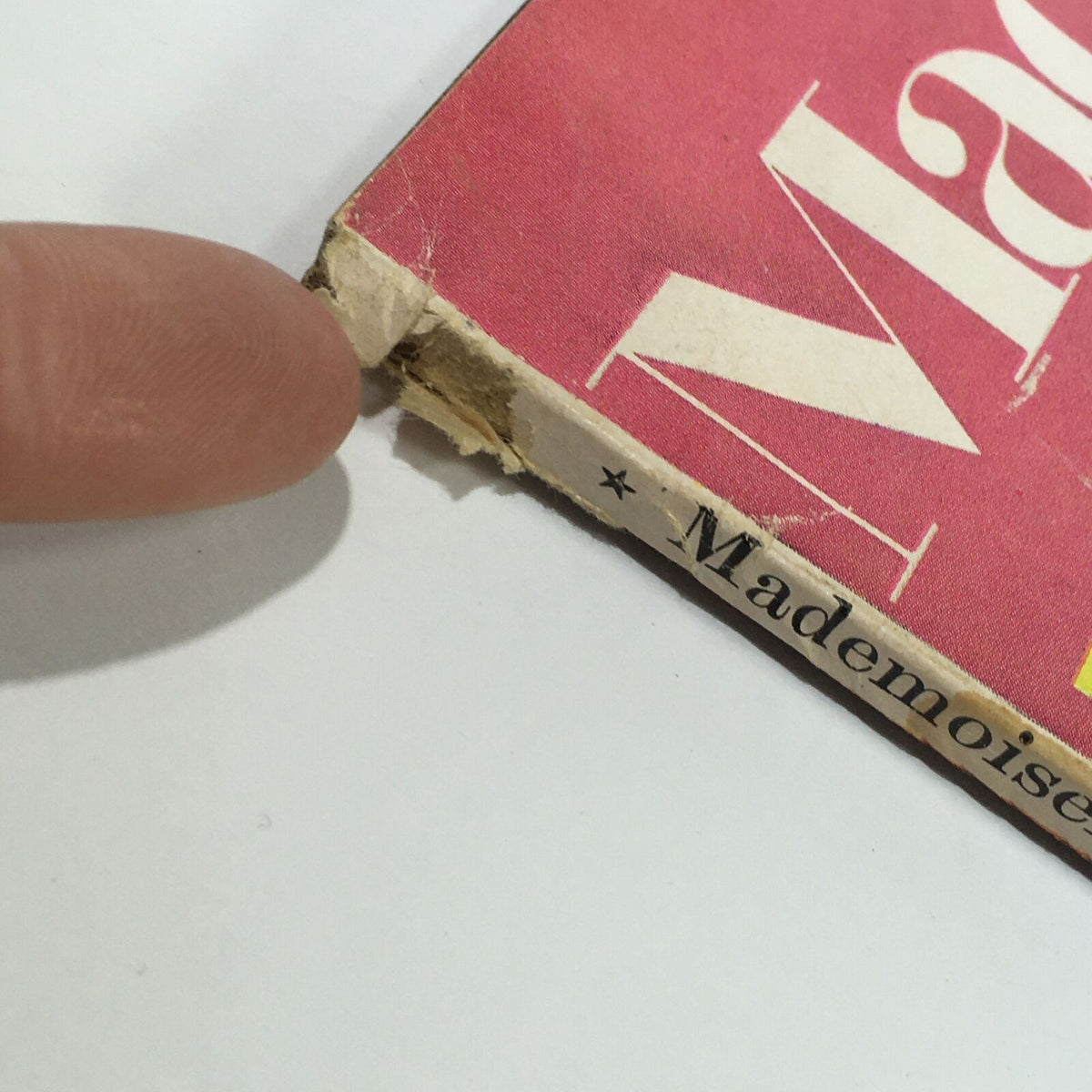 Close-up of the corner of the vintage Mademoiselle Magazine from December 1967, showcasing its wear and vintage character, highlighting the title and a finger pointing at the damaged area.