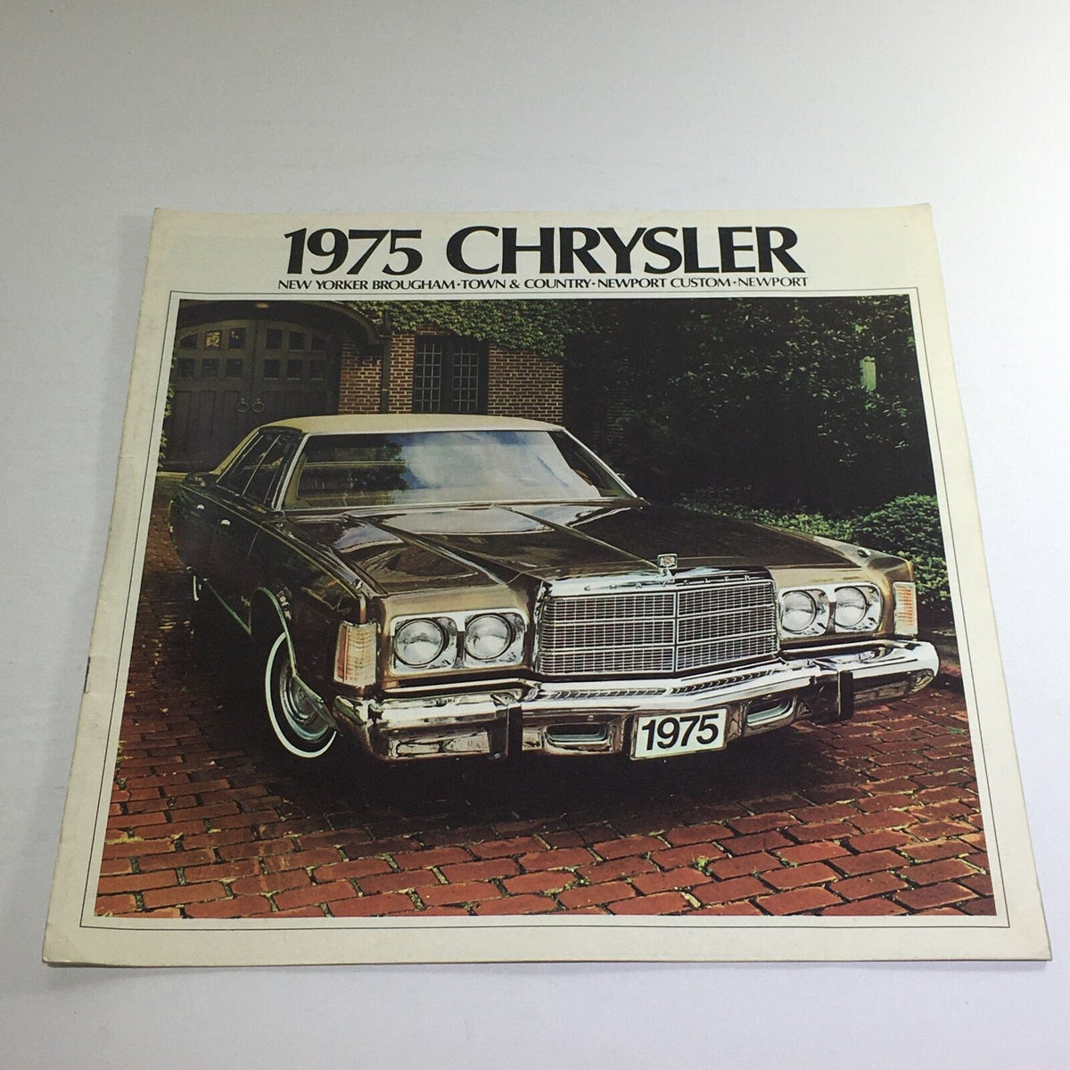 1975 Chrysler New Yorker Brougham Dealership Car Auto Brochure featuring an elegant exterior shot of the vehicle in a lush outdoor setting.