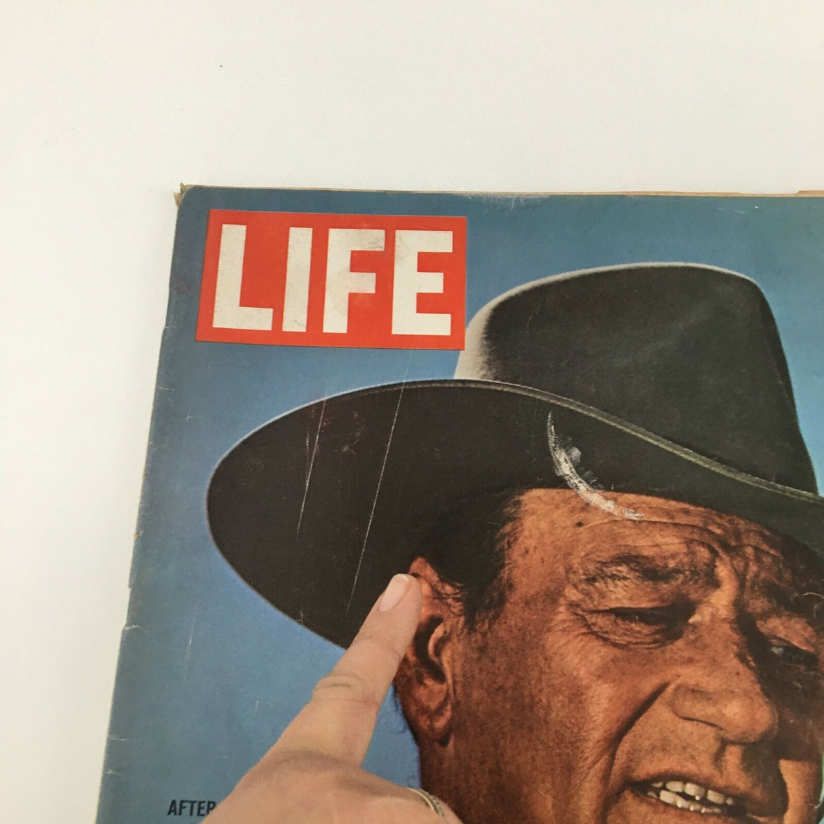 Close-up of the Vintage Life Magazine cover from May 7, 1965, highlighting John Wayne after his battle with cancer, with a finger pointing to the magazine's details and the title clearly visible.
