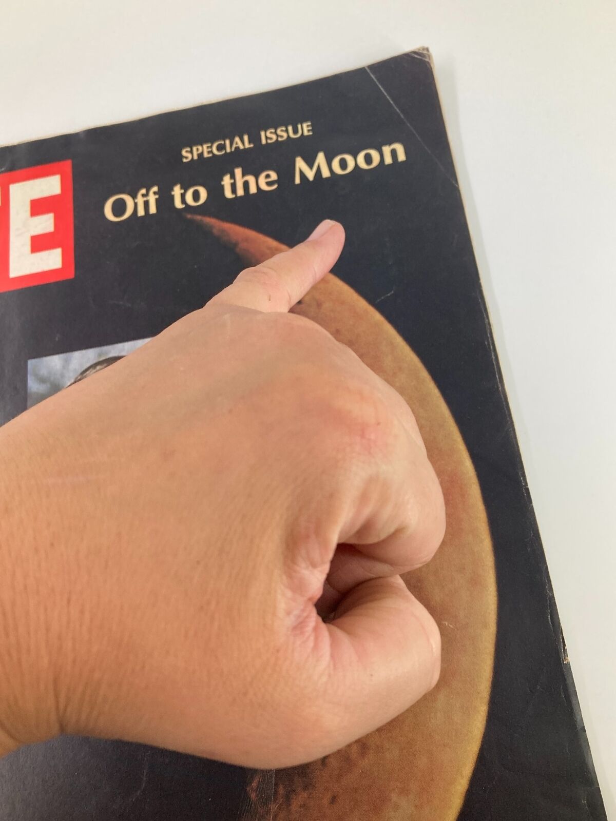 Close-up view of the July 4, 1969 edition of Life Magazine, highlighting the title 'Off to the Moon' with a hand pointing at the cover. This special issue commemorates Neil Armstrong's historic lunar landing.