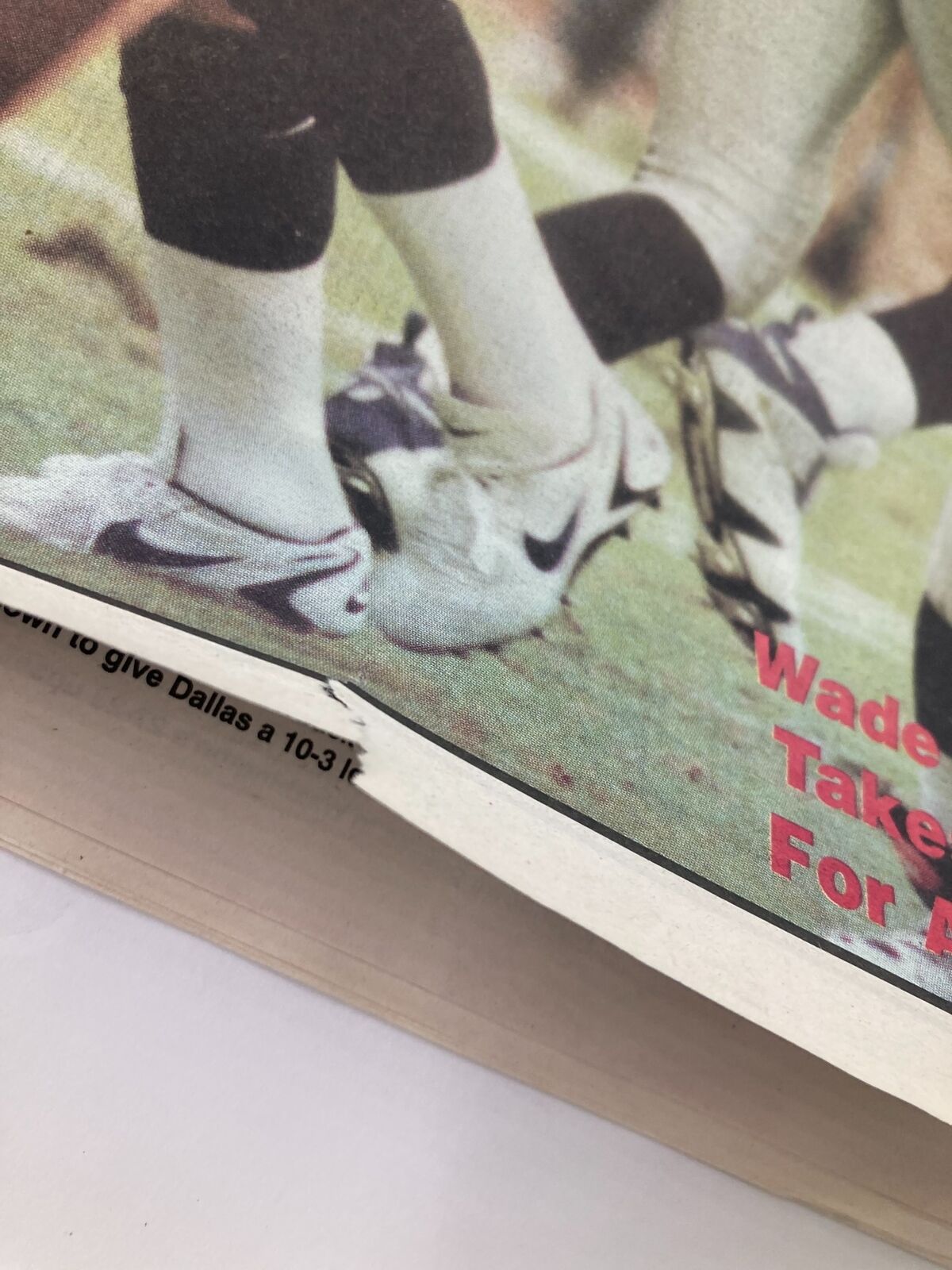 Detail view of the bottom edge of the Dallas Cowboys Weekly Newspaper showing creased edges and the headline regarding Wade Wilson.