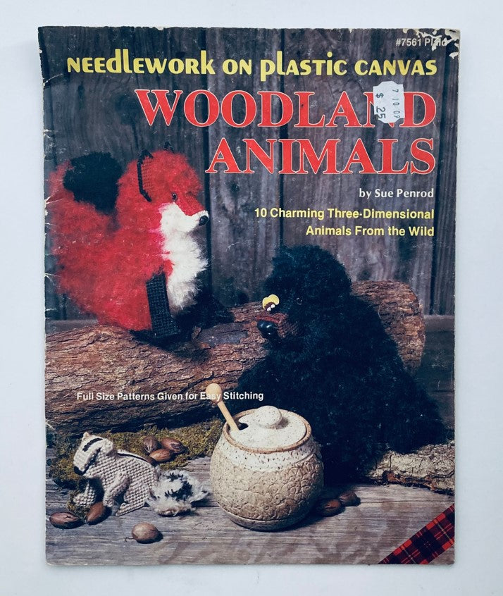 Cover of the book titled 'Needlework on Plastic Canvas Woodland Animals' by Sue Penrod, featuring a red fox and a black bear with a rustic background, showcasing 10 charming three-dimensional animals from the wild.