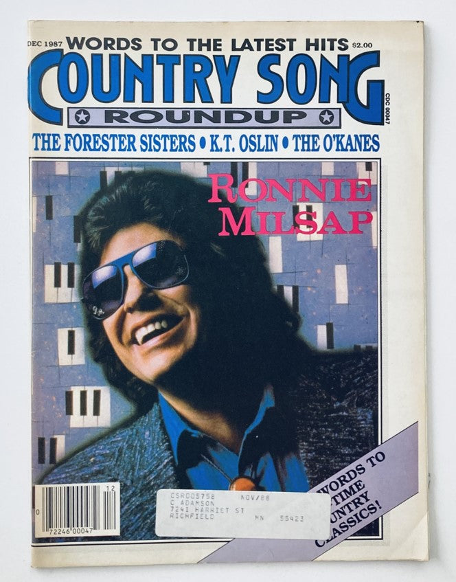 Cover of VTG Country Song Roundup Magazine December 1987 featuring a smiling Ronnie Milsap, wearing sunglasses and a stylish outfit, with musical notes and text highlighting the artists in the edition including K.T. Oslin and The Forester Sisters.