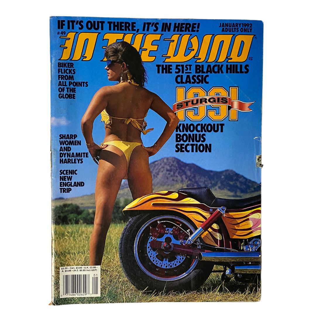 In The Wind Magazine January 1992 No. 49 featuring a woman in a yellow bikini posing beside a motorcycle with vibrant flames, highlighting biker culture and activities from the Sturgis Classic in the Black Hills.