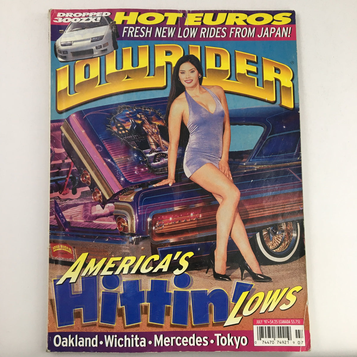 Cover of LowRider Magazine July 1997 featuring the title 'America Hittin' Low' with a model in a silver outfit posing beside a custom lowrider car, showcasing lowrider culture and style.