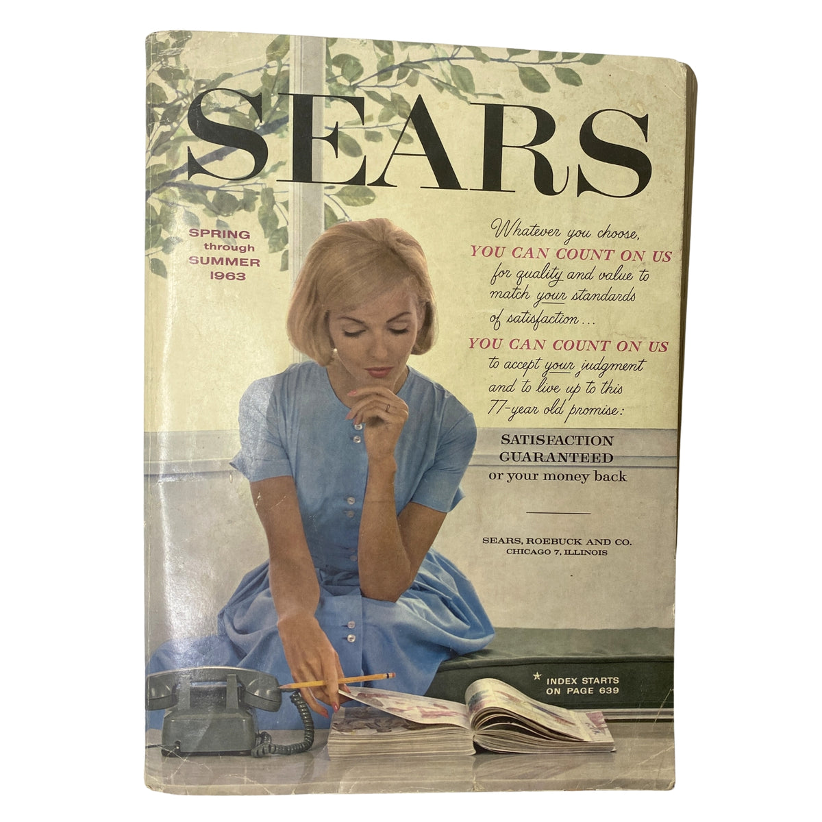 Cover of the 1963 Sears Classic Spring and Summer Catalog featuring a woman in a blue dress, seated with a telephone and a pencil, surrounded by greenery. The catalog emphasizes quality and satisfaction.