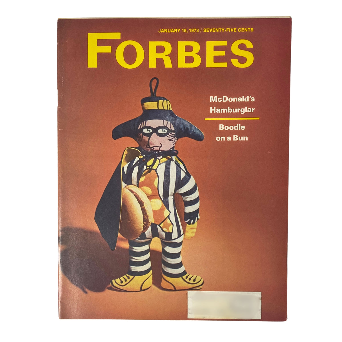 Forbes Magazine cover from January 15, 1973, featuring McDonald's Hamburglar Boodle on a Bun, showcasing a playful character in a striped outfit holding a hamburger, set against a warm, brown background.