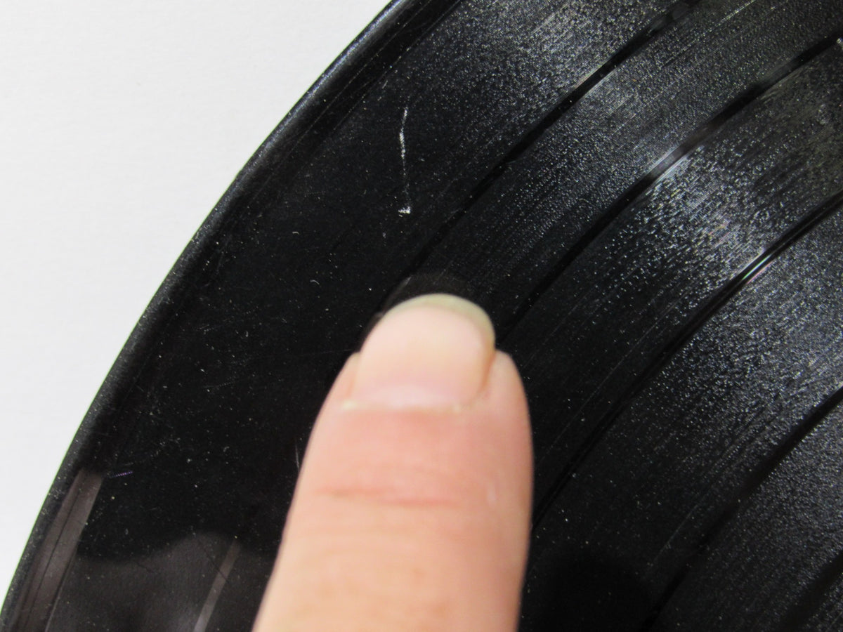 Detailed close-up of The Beatles: Meet The Beatles US Mono Capitol Records LP T 2047 record surface, highlighting a finger pointing at a scratch on the vinyl.