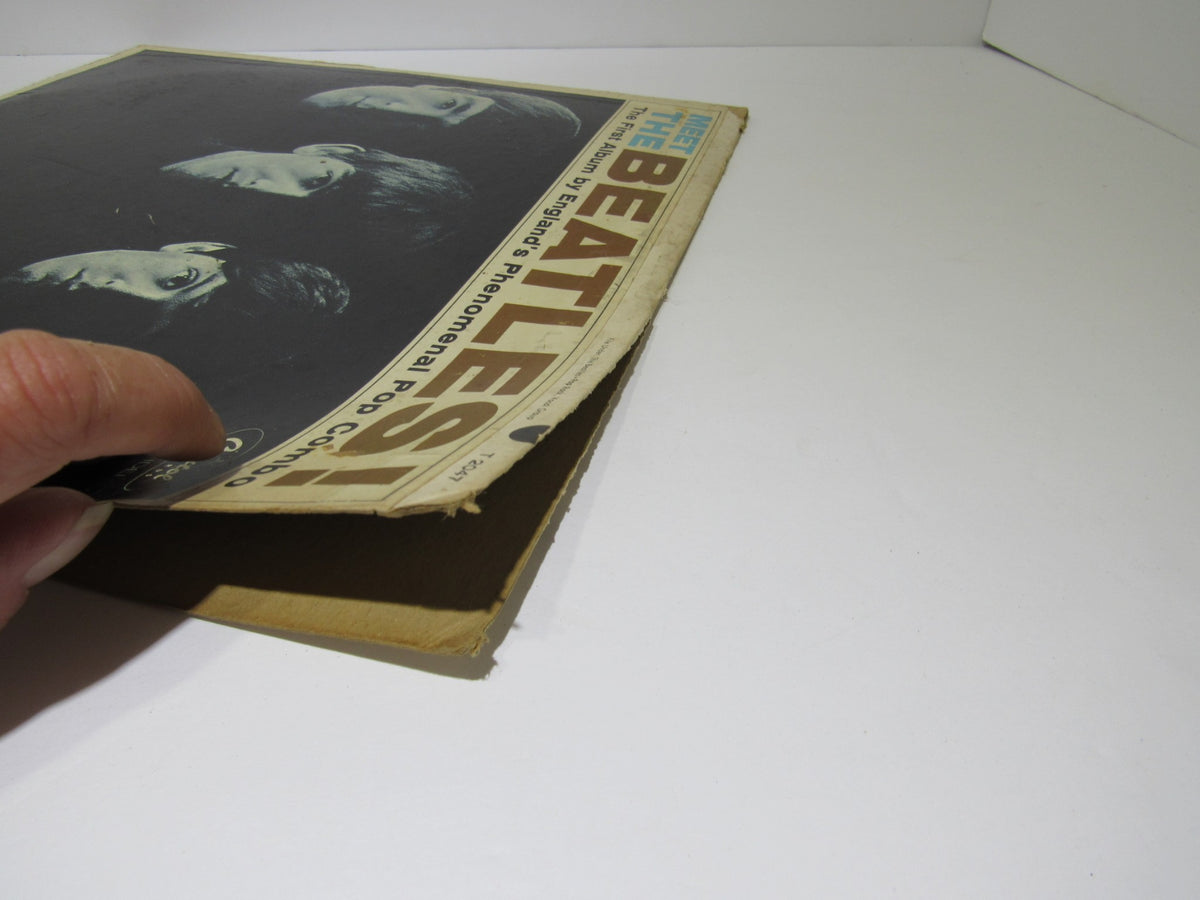 Close-up of the cover of 'The Beatles: Meet The Beatles US Mono Capitol Records LP T 2047 Grade: G' showing cover wear and a hand holding the record.