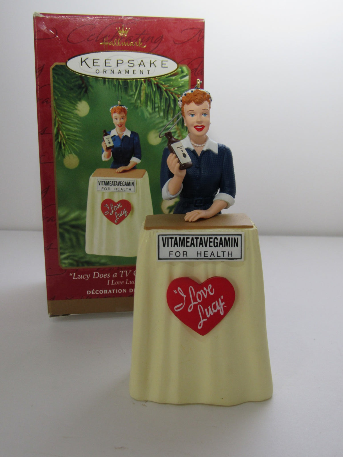 2001 Hallmark Keepsake Ornaments I Love Lucy VitaMeataVegamin featuring a figurine of Lucy holding a health tonic bottle with a skirt design, displayed in its original box.