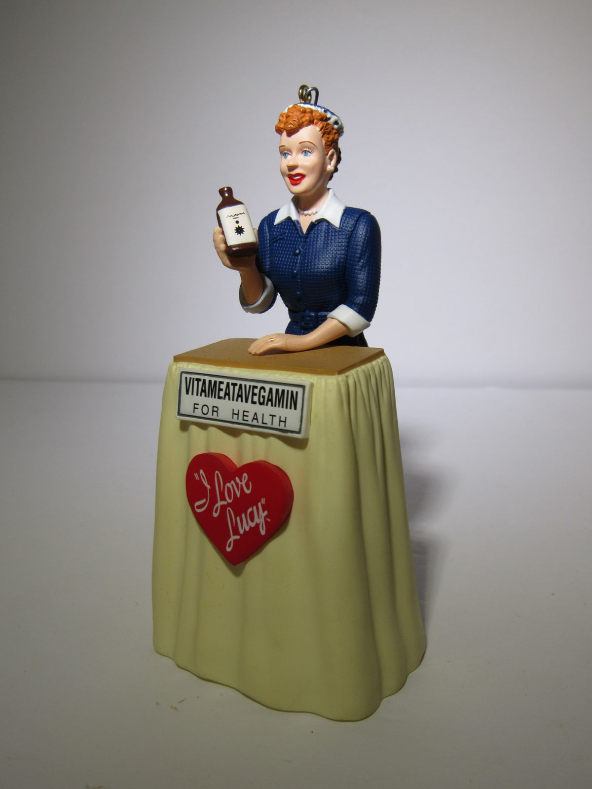 2001 Hallmark Keepsake Ornaments I Love Lucy VitaMeataVegamin showcasing a detailed figurine of Lucy with a tonic bottle and a signature heart logo, presented without the box.