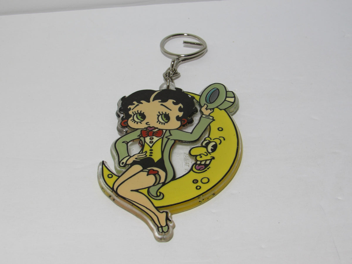 1985 Rare Vintage Betty Boop On the Moon Key Chain featuring Betty Boop sitting on a crescent moon, adorned in a tuxedo with a bowtie, with a playful expression and a whimsical design, ideal for collectors of vintage memorabilia.