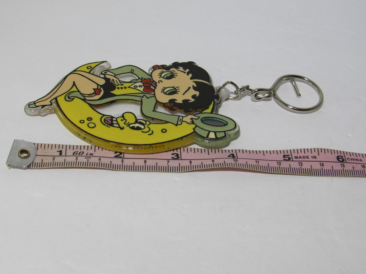 1985 Rare Vintage Betty Boop On the Moon Key Chain displayed with a measuring tape for size comparison, showcasing Betty Boop lounging on a yellow crescent moon.