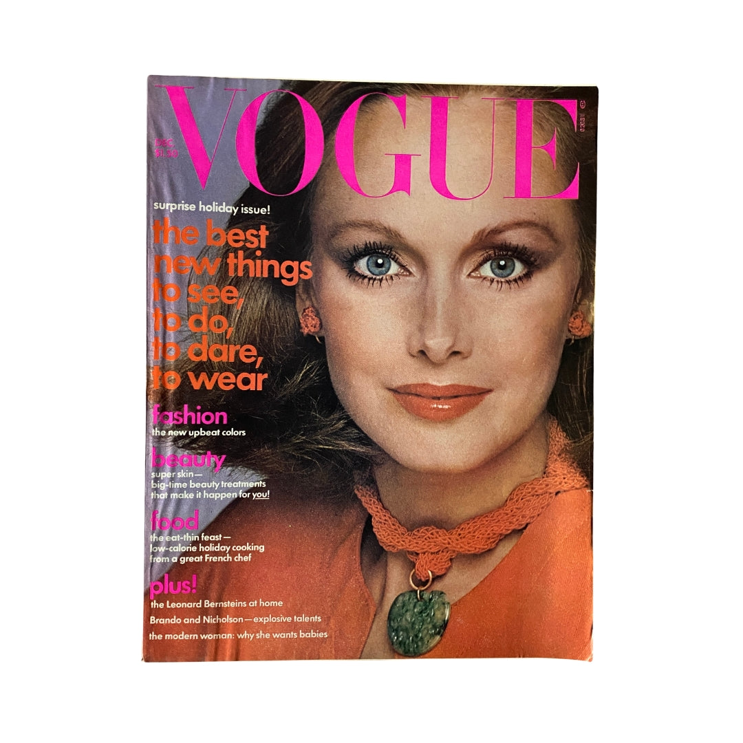 Vogue Magazine December 1975 Karen Graham Cover showcasing a stunning model with striking blue eyes, wearing orange lipstick and fashionable jewelry against a vibrant pink and orange title. This magazine highlights the best trends in fashion, beauty, and food for the holiday season.