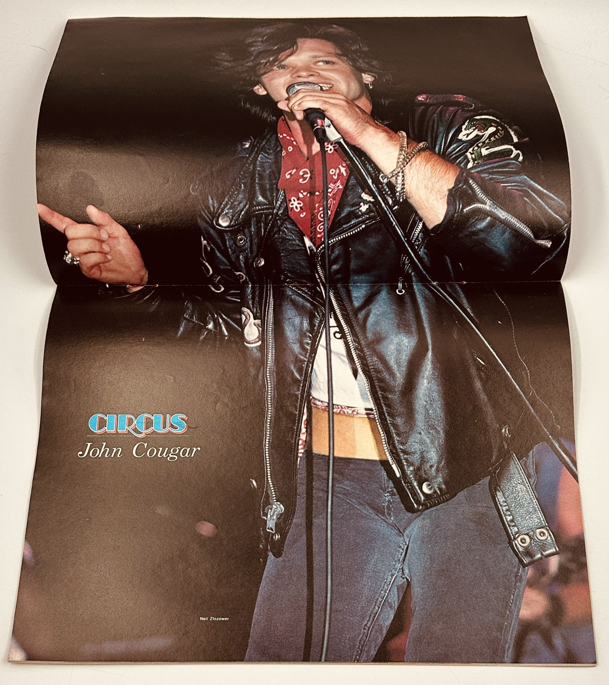 Full-page poster of John Cougar from Circus Magazine, November 30, 1982, showcasing the artist in a leather jacket during a live performance, promoting his music and latest album.