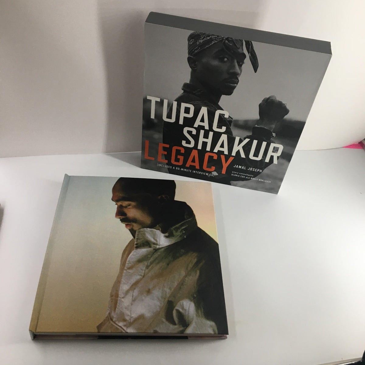 Tupac Shakur Legacy book cover featuring Tupac in a black bandana and jacket with the title prominently displayed in bold orange letters.