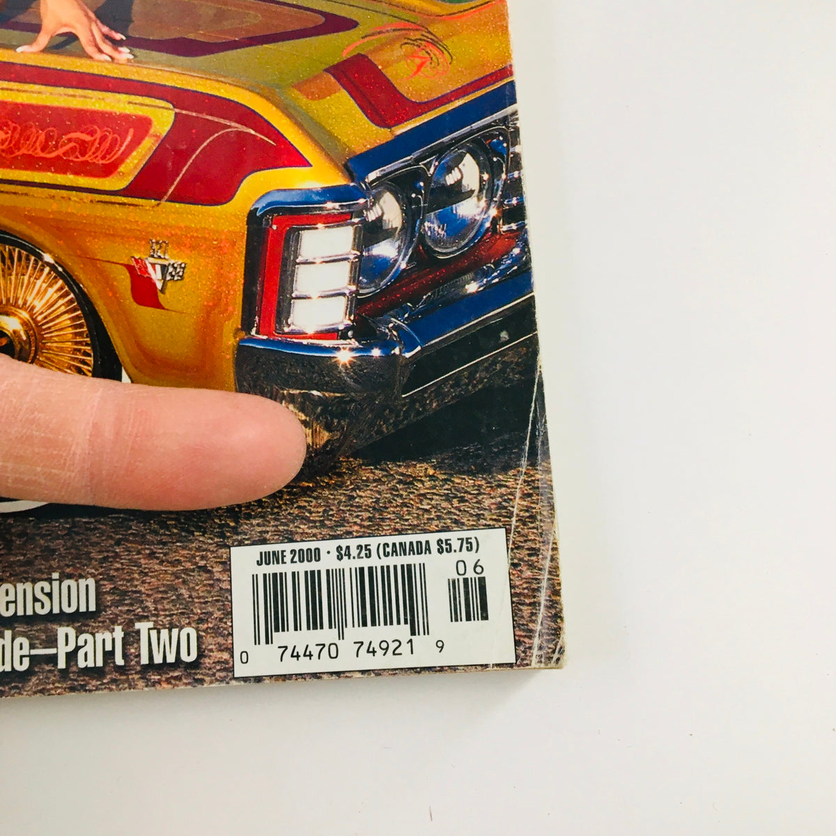 Close-up of the LowRider Magazine June 2000 edition, highlighting the feature of Wild West Ridaz with colorful lowrider car details and a finger pointing at the magazine's cover rear.