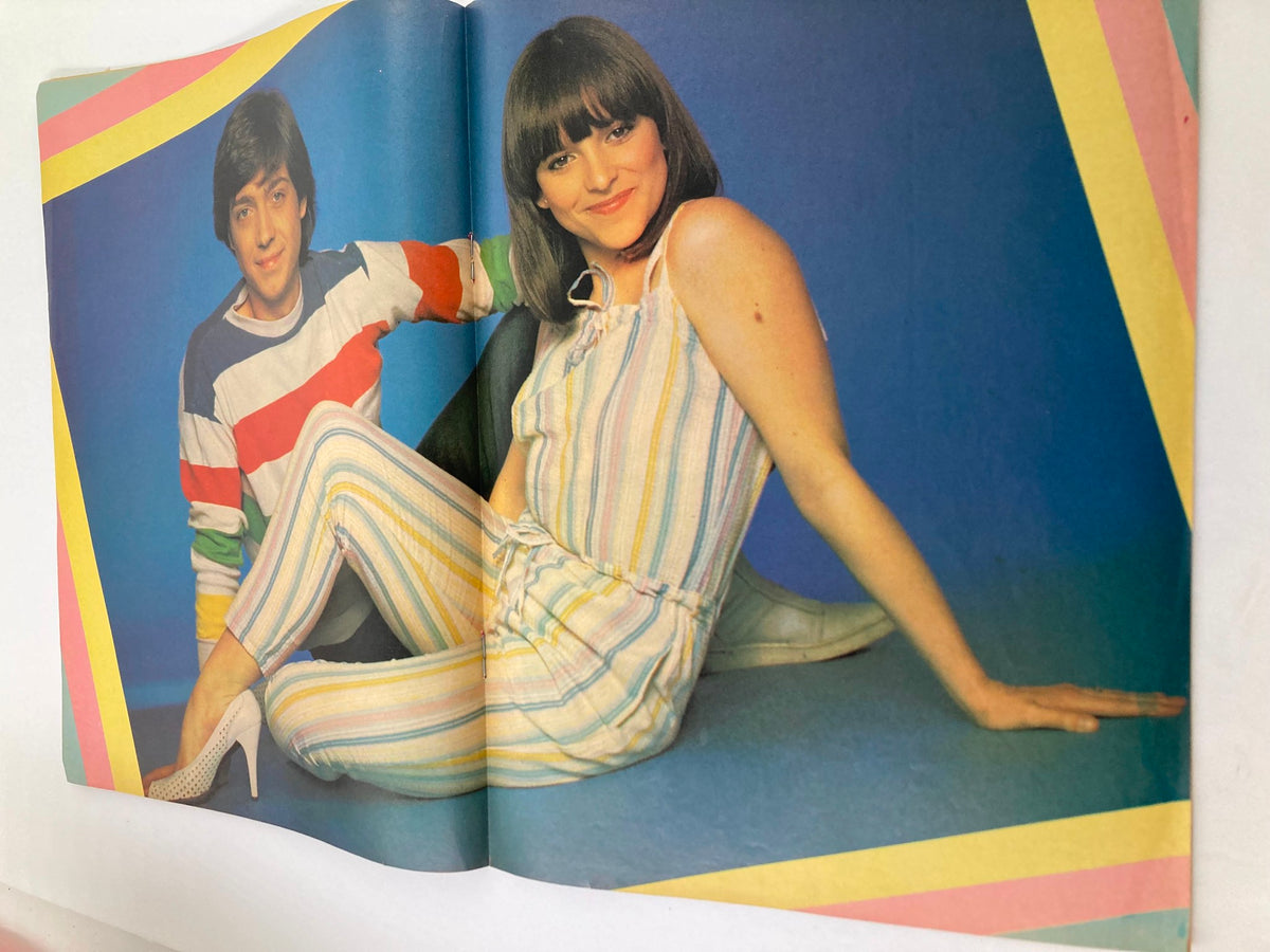 Inside spread of VTG Lookin Magazine May 15 1982 #20, showcasing a vibrant photo of two young people in trendy outfits, set against a bright blue backdrop with geometric accents.