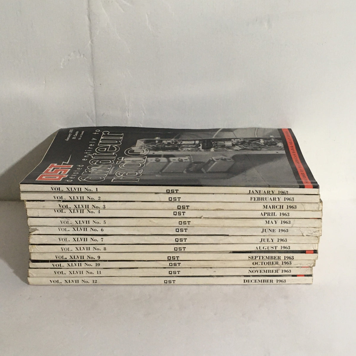 Lot of 12 Complete January to December 1963 QST Amateur Radio Volume 1-12 with an arranged view of the magazine spines featuring publication dates and volume details.