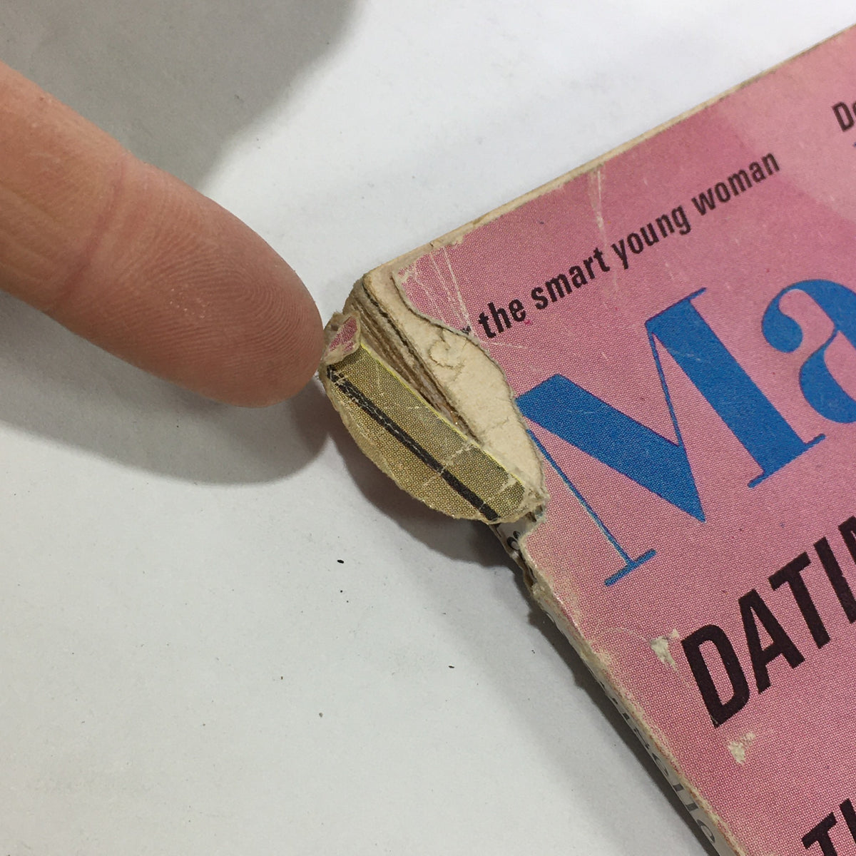 Close-up of VTG Mademoiselle Magazine: December 1965 showing wear on the spine, illustrating the vintage condition of this collector's item.