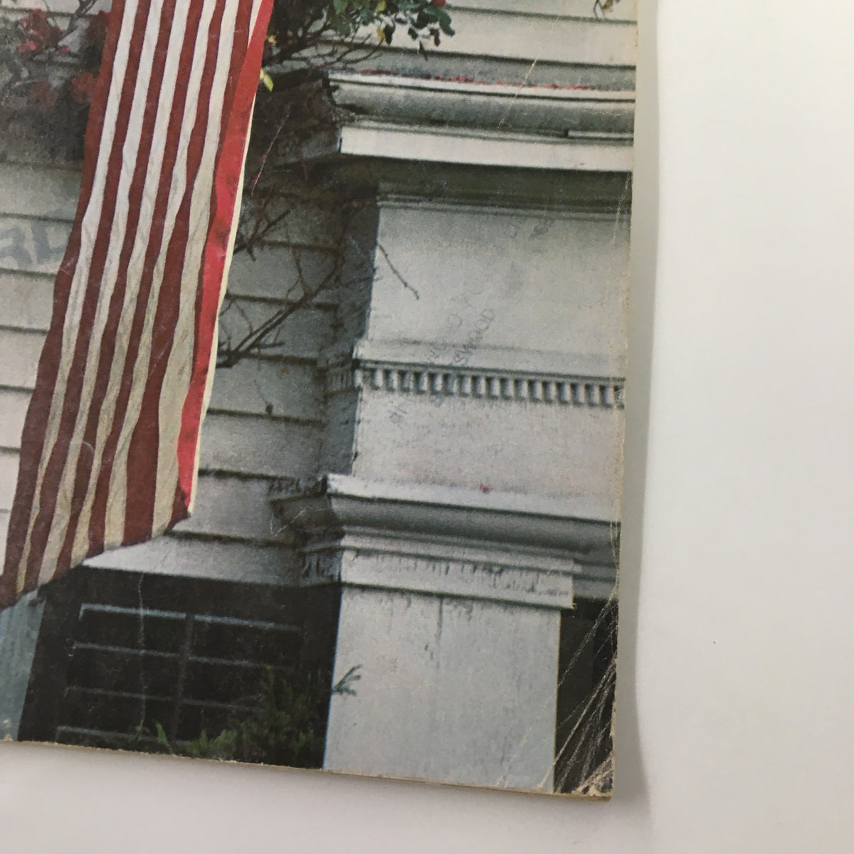American flag hanging from a house, featured in VTG Gourmet Magazine July 1976 titled 'Flag-Waving As We Pay Tribute'.