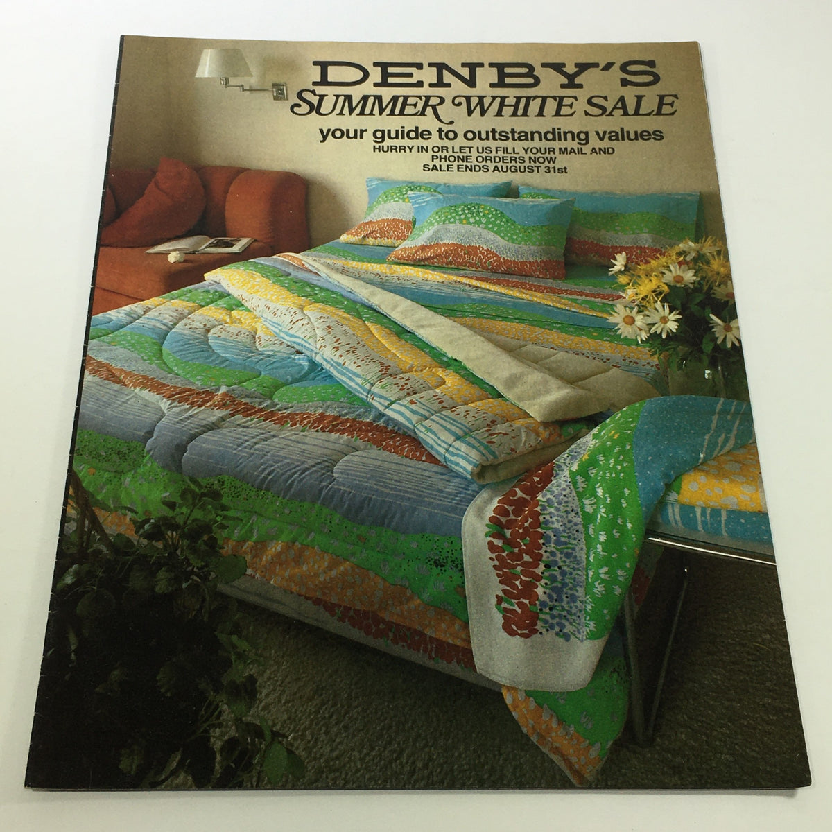 VTG Denby's Catalog: 1980s - Summer White Sale Guide featuring a colorful quilted bedspread and decorative pillows on a bed, promoting outstanding values, with a welcoming living room background.