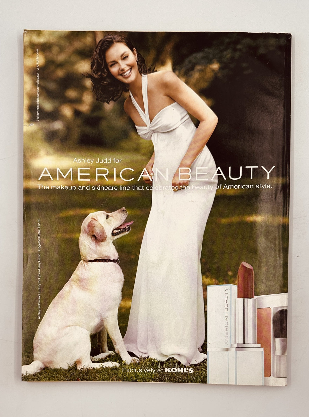 Advertisement featuring Ashley Judd for American Beauty, promoting a skincare line, showcasing a model in a white dress with a dog, emphasizing themes of beauty and American style.