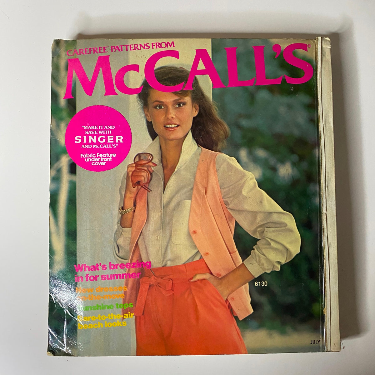 1977 July Carefree Patterns from McCall's Summer Catalog cover image featuring a model in a stylish outfit with vibrant pink lettering and tropical background, showcasing summer fashion inspirations.