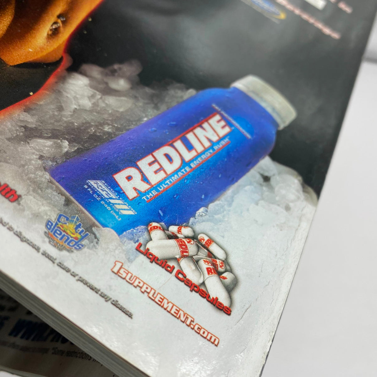 Close-up view of the Redline supplement featured in the Muscular Development Magazine April 2006, illustrating its packaging with the blue bottle and capsules within an ice setting.