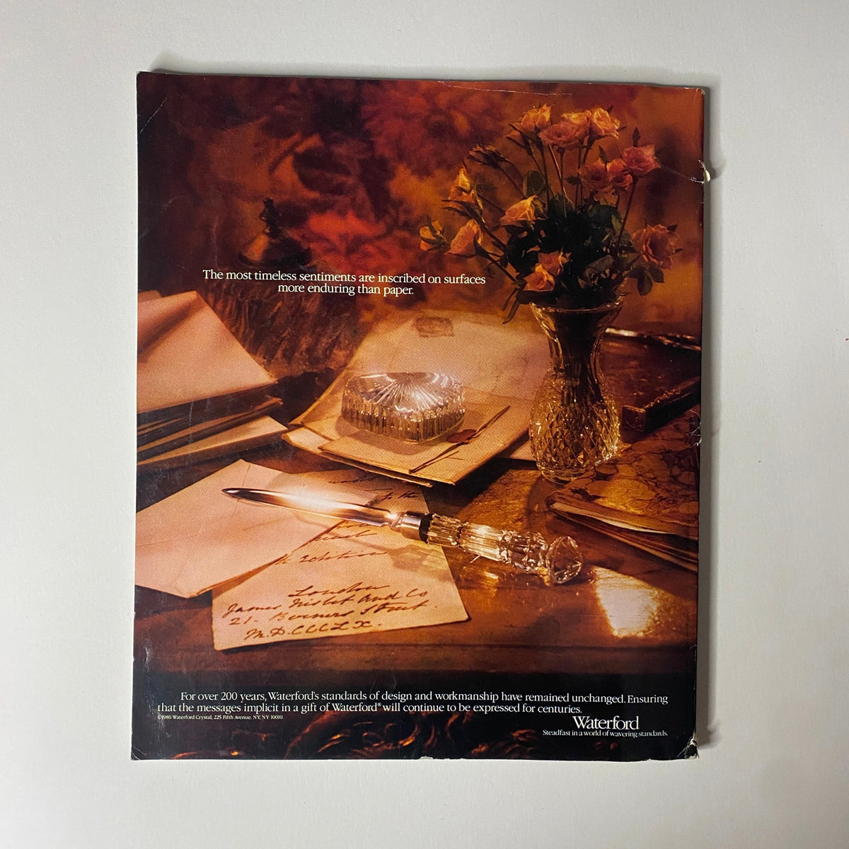 An advertisement featuring elegant stationery, a crystal inkstand, and roses that conveys the sentiment 'The most timeless sentiments are inscribed on surfaces more enduring than paper.' This image promotes Waterford, reflecting craftsmanship and elegance in writing. Connoisseur Magazine March 1987 The Unknown British Museum No Label.
