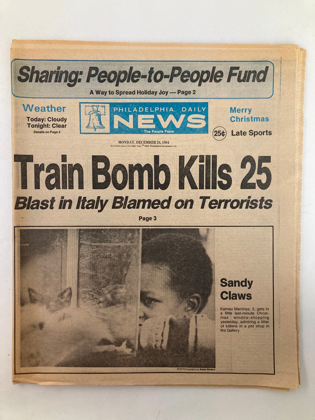 Philadelphia Daily News Tabloid December 24 1984 featuring a headline about a train bomb incident that killed 25, with an image of Kamau Martinez depicted as Sandy Claws. The tabloid includes festive holiday elements and news content.