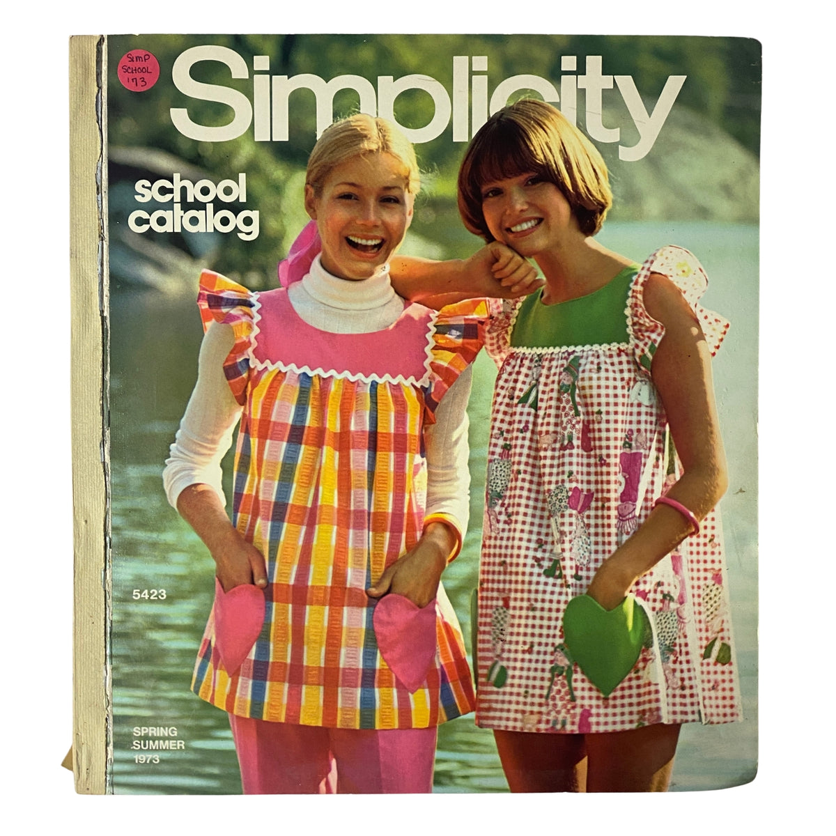 Vintage 1973 Simplicity Spring Summer School Catalog featuring two models, one in a colorful checked dress and the other in a floral print dress, both showcasing trendy styles for young home sewers.