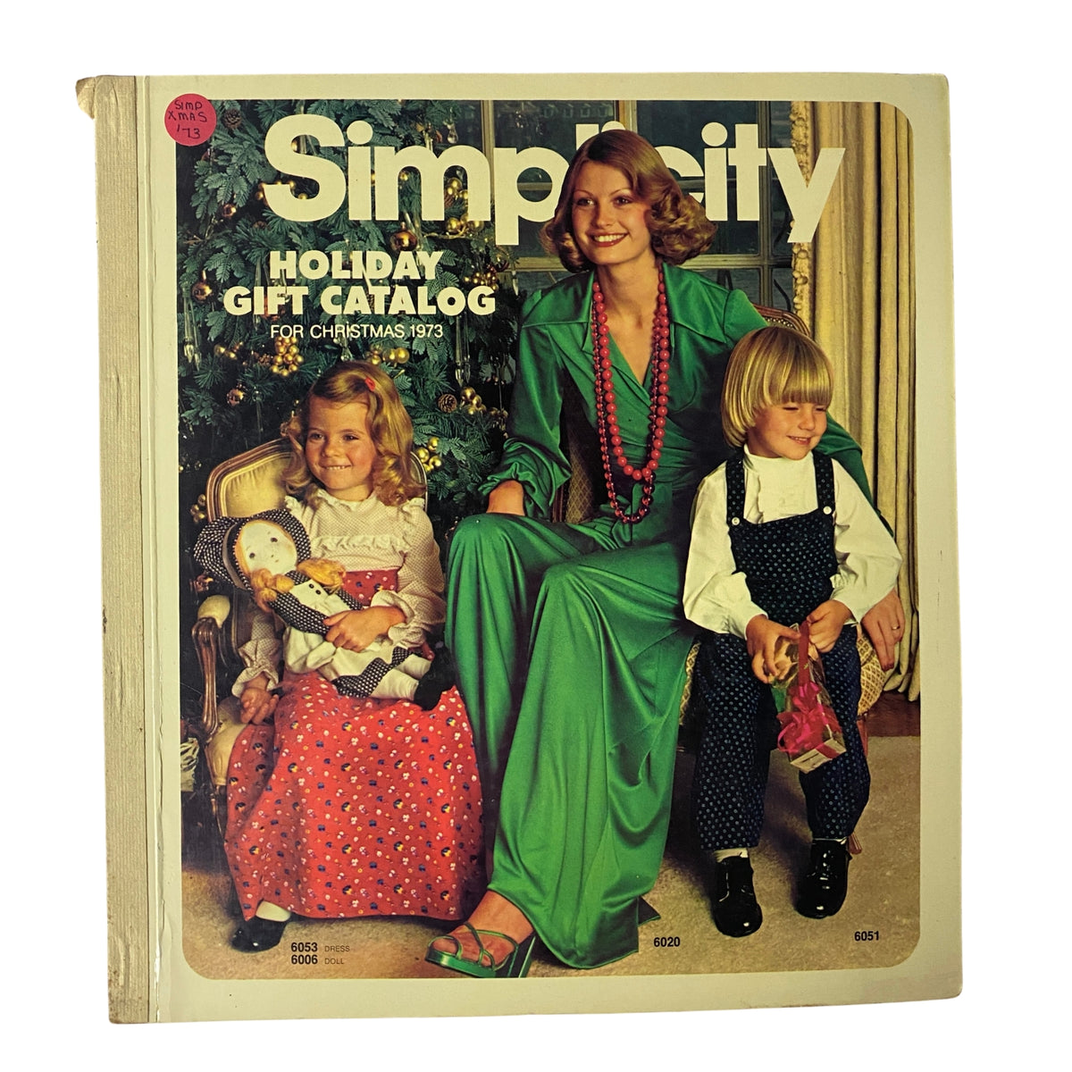 1973 Simplicity Holiday Gift Catalog featuring a woman in a green dress surrounded by children, showcasing festive holiday fashion and sewing patterns.