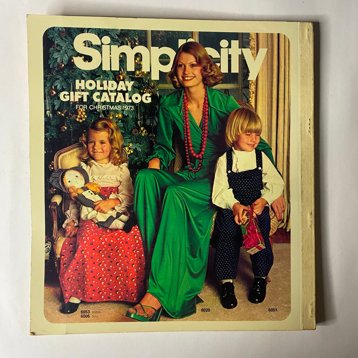 1973 Simplicity Holiday Gift Catalog cover featuring a woman in a green dress with two children, showcasing the spirit of holiday fashion and creativity in handmade gifts.