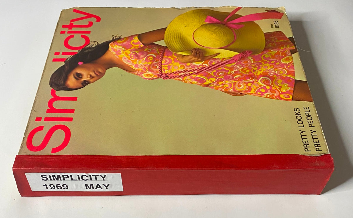 Side view of the 1969 May Simplicity Catalog highlighting the title 'Simplicity 1969 May', featuring a model wearing a vibrant dress and holding a hat.