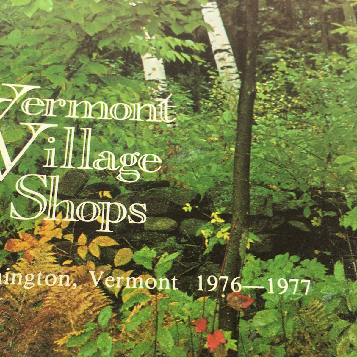 Close-up detail of the VTG Vermont Village Shops Catalog: 1976 - 1977 showcasing the title and subtitle against a backdrop of greenery.