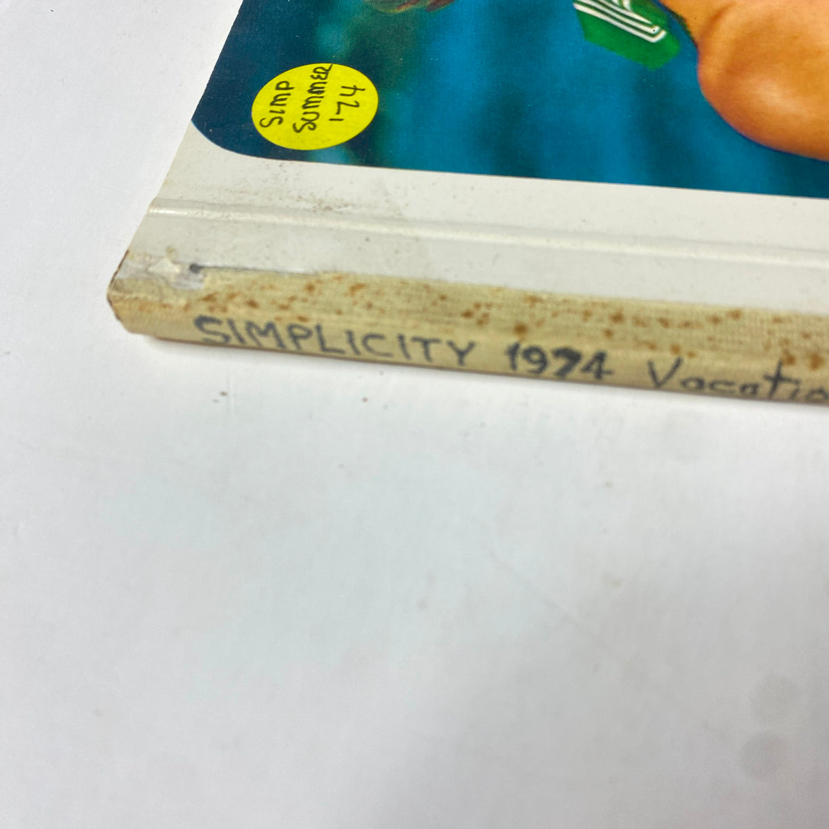 Close-up view of the spine of the 1974 Simplicity Summer Catalog, displaying the handwritten note 'Simplicity 1974 Vacation Summer' and a sticker.