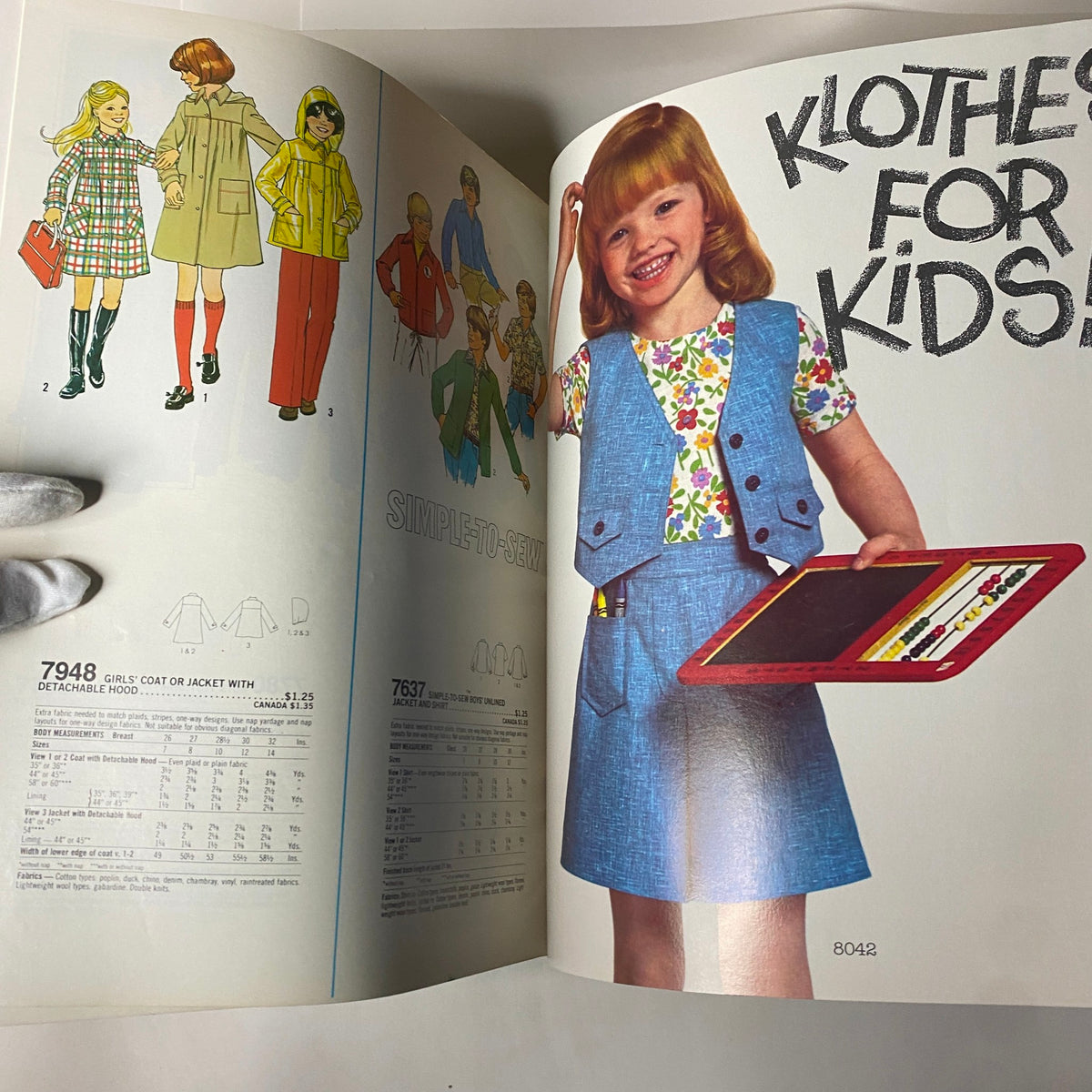 Page from the 1977 Simplicity Fall Catalog titled 'Clothes for Kids'; featuring a smiling child in a vest holding a drawing board, alongside detailed sewing patterns for kids' clothing.