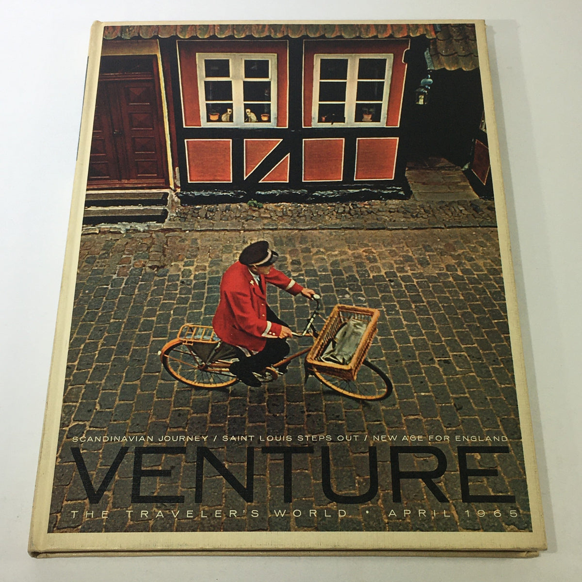 Cover of VTG Venture Magazine Book: April 1965, featuring a man in a red coat riding a bicycle in front of traditional buildings, highlighting Scandinavian culture, Saint Louis, and England.